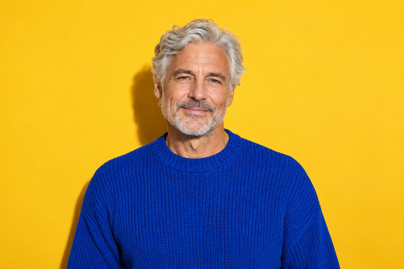 A silver-haired man in a cobalt knit against yellow