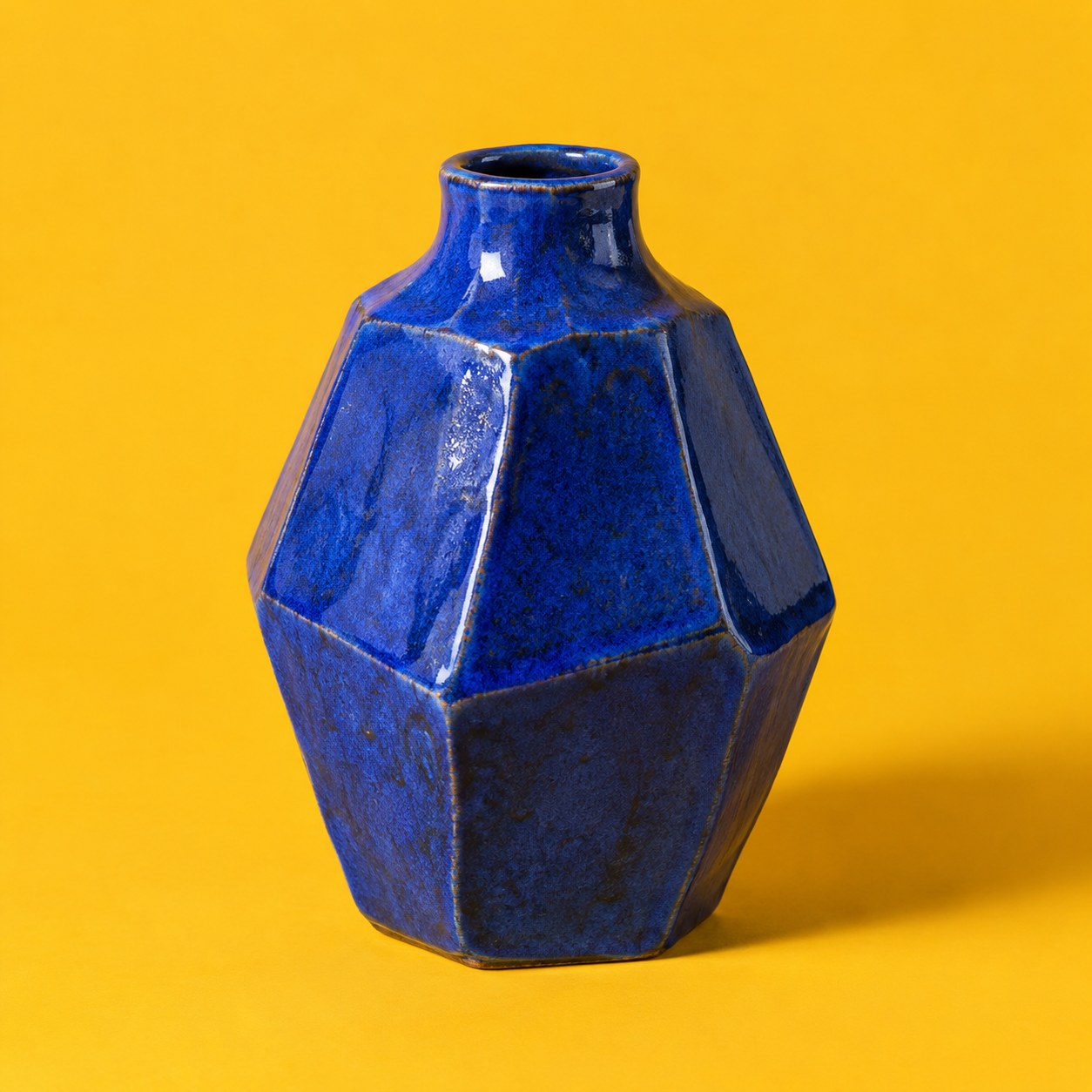An angular cobalt ceramic vase against marigold yellow