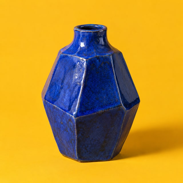 An angular cobalt ceramic vase against marigold yellow