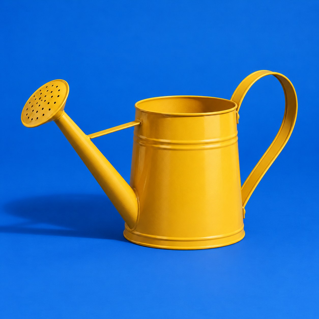 A marigold watering can on a cobalt backdrop