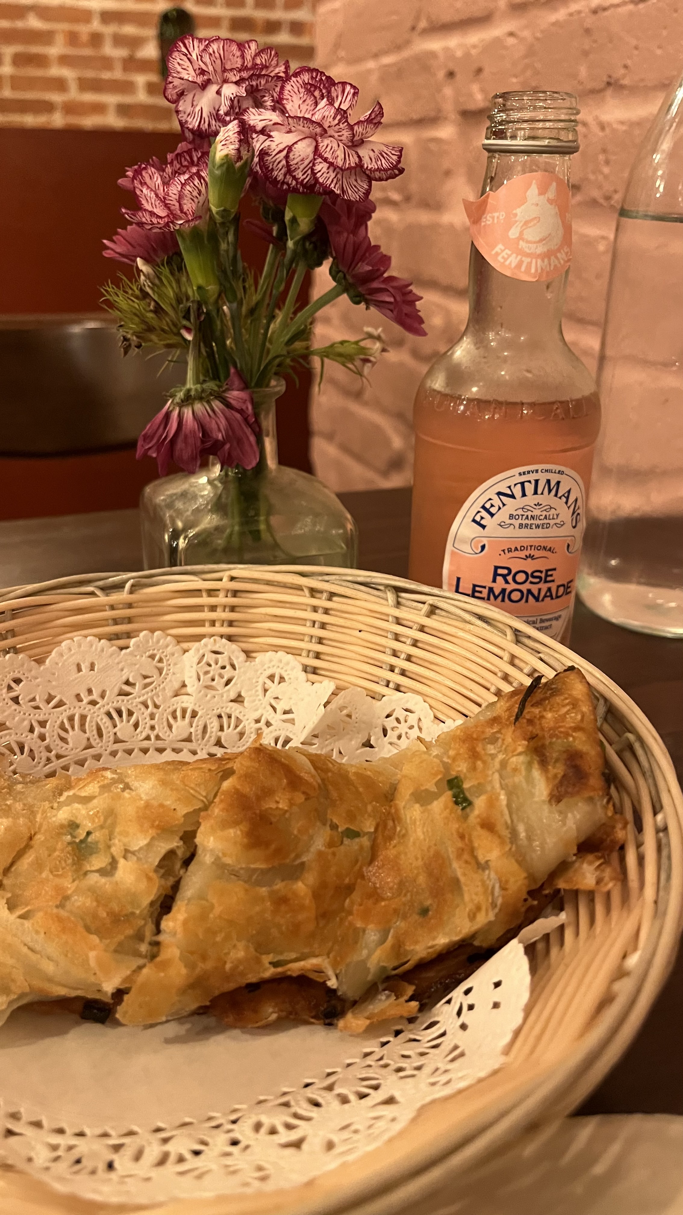 A pastry basket beside flowers and rose lemonade.