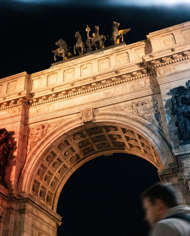 A triumphal arch crowned with statues at night, made by Muse.